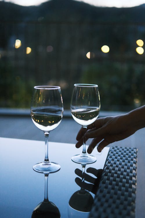 Two wine glasses on a table with a person's hand