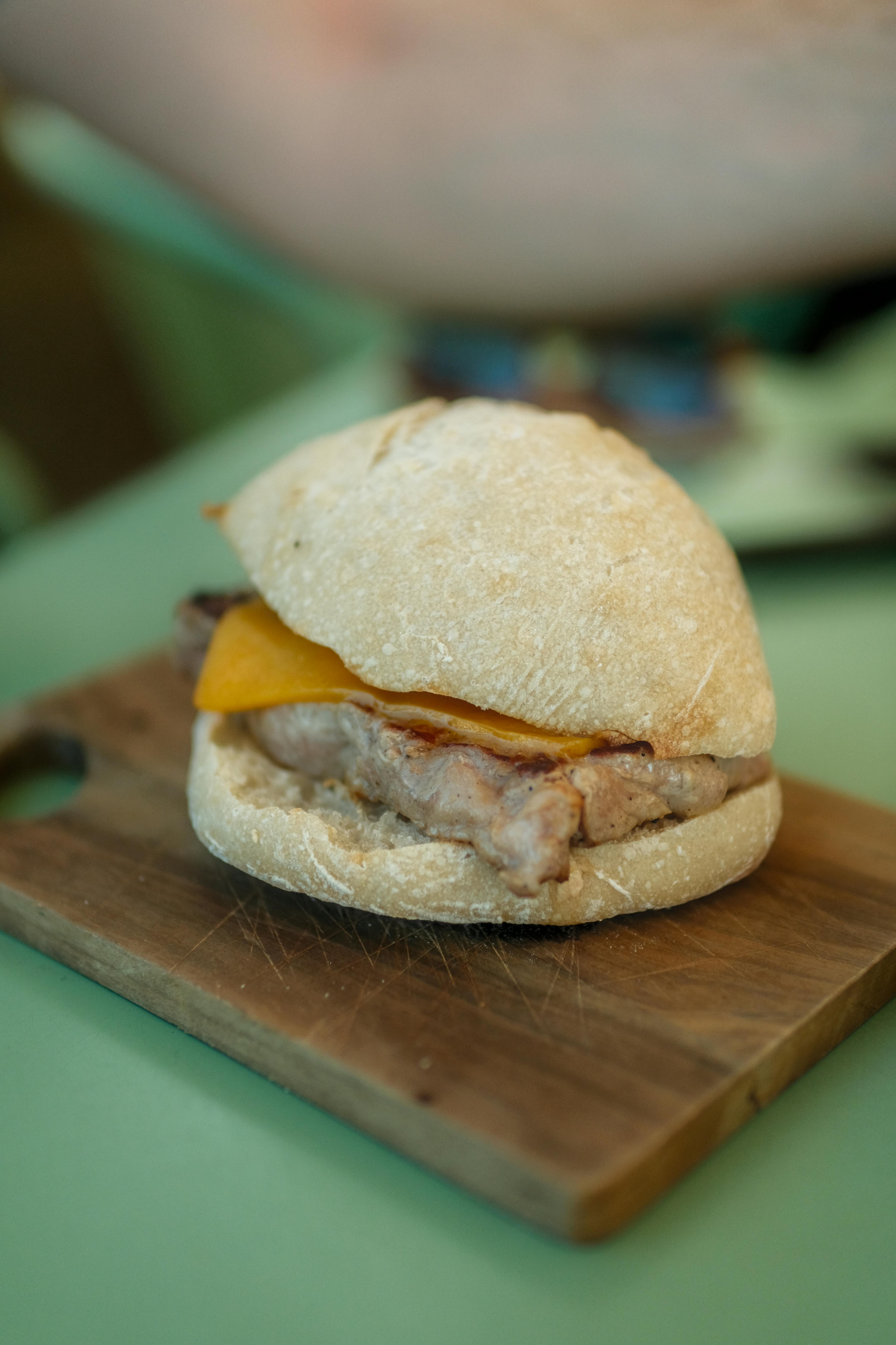Close-up of a homemade burger with cheese on a wooden cutting board, ideal for food enthusiasts.
