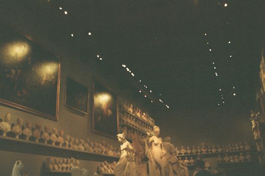 Dimly lit museum gallery showcasing sculptures, busts, and classical paintings.