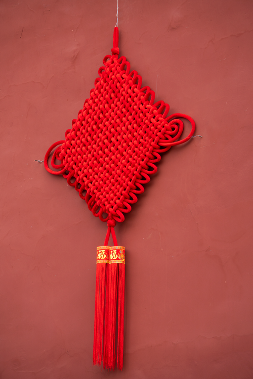 Free Red Chinese knot hanging on a wall, symbolizing luck and prosperity. Stock Photo