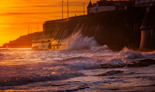 Free Vibrant sunset over the ocean with waves crashing on a coastal wall. Stock Photo