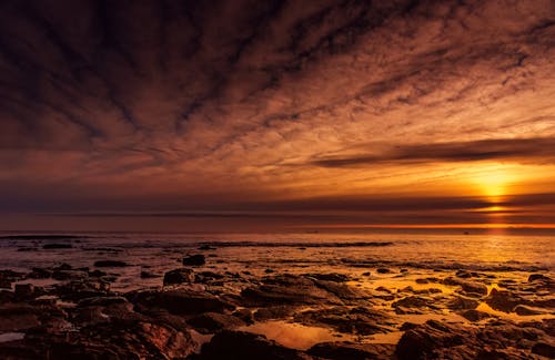 A sunset over the ocean with rocks and clouds