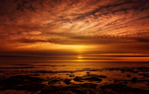 A sunset over the ocean with clouds and rocks