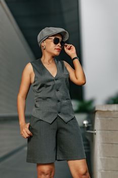 Fashionable woman wearing a grey vest and shorts, posing confidently outdoors.