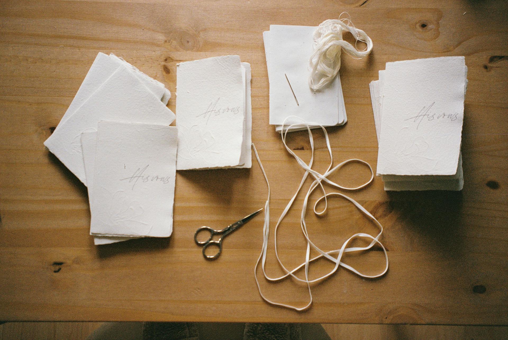 A flat lay of handmade paper craft supplies with scissors and thread on a wooden desk.