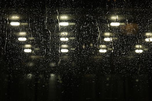 Glistening raindrops on glass with blurred urban lights create a moody night ambiance.