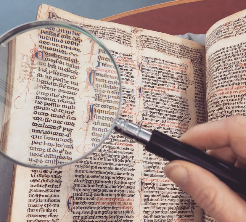 Person Holding Magnifying Glass Pointing on Book