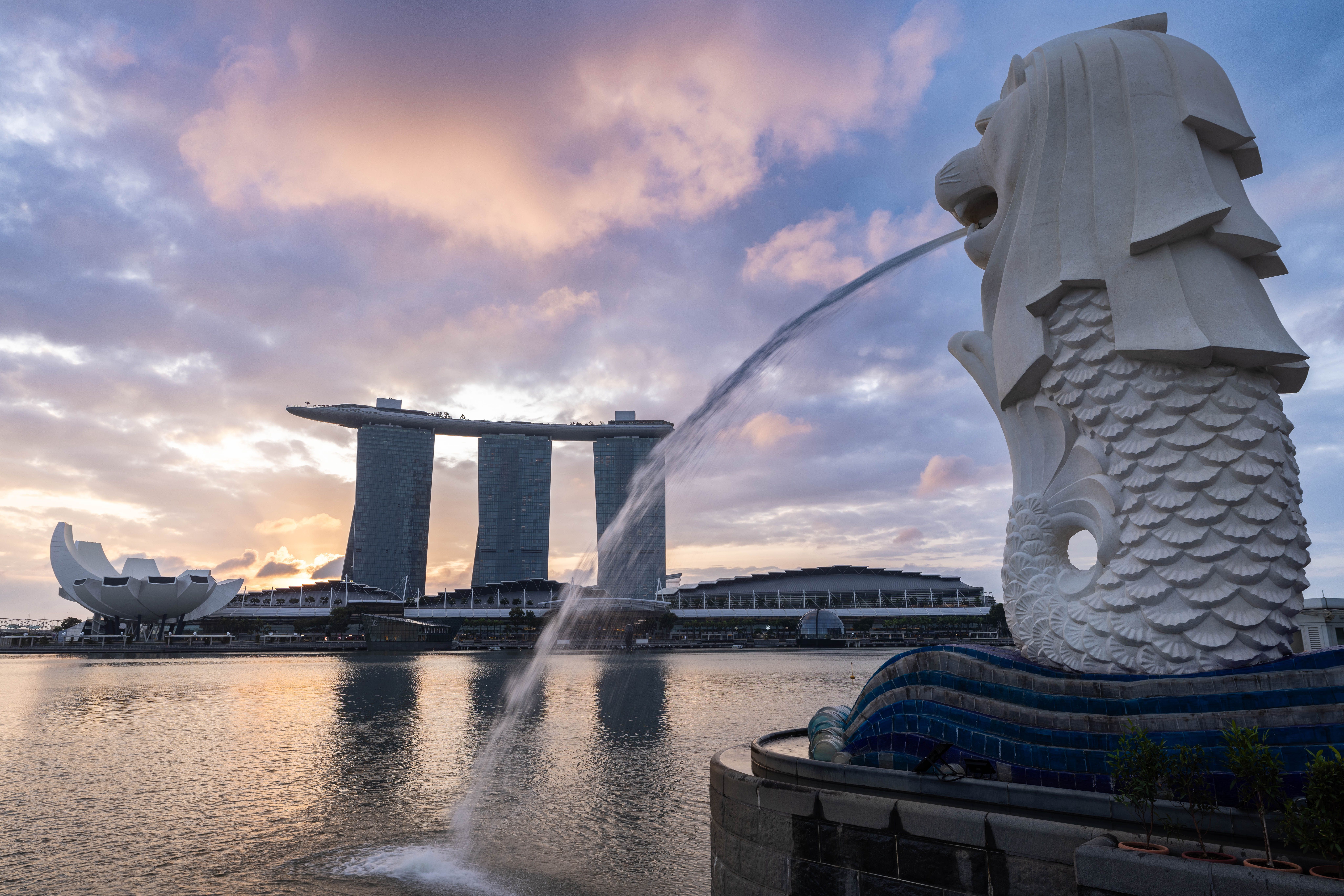 Marina Bay Sands three hotel towers lit up at dusk viewed from Merlion Park across the bay in Singapore