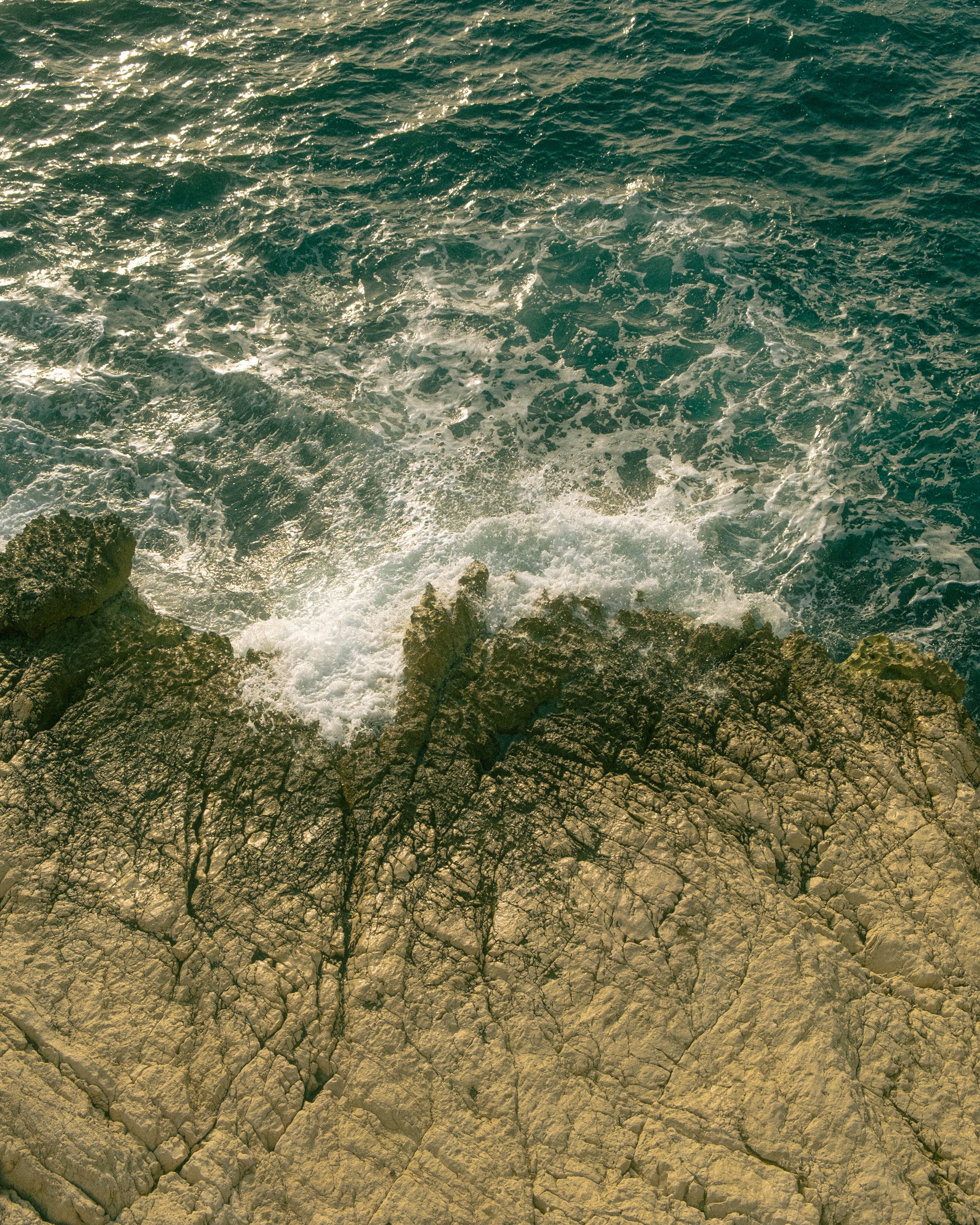 Stunning aerial view of a rocky coastline with waves crashing on the shore, showcasing natural beauty.