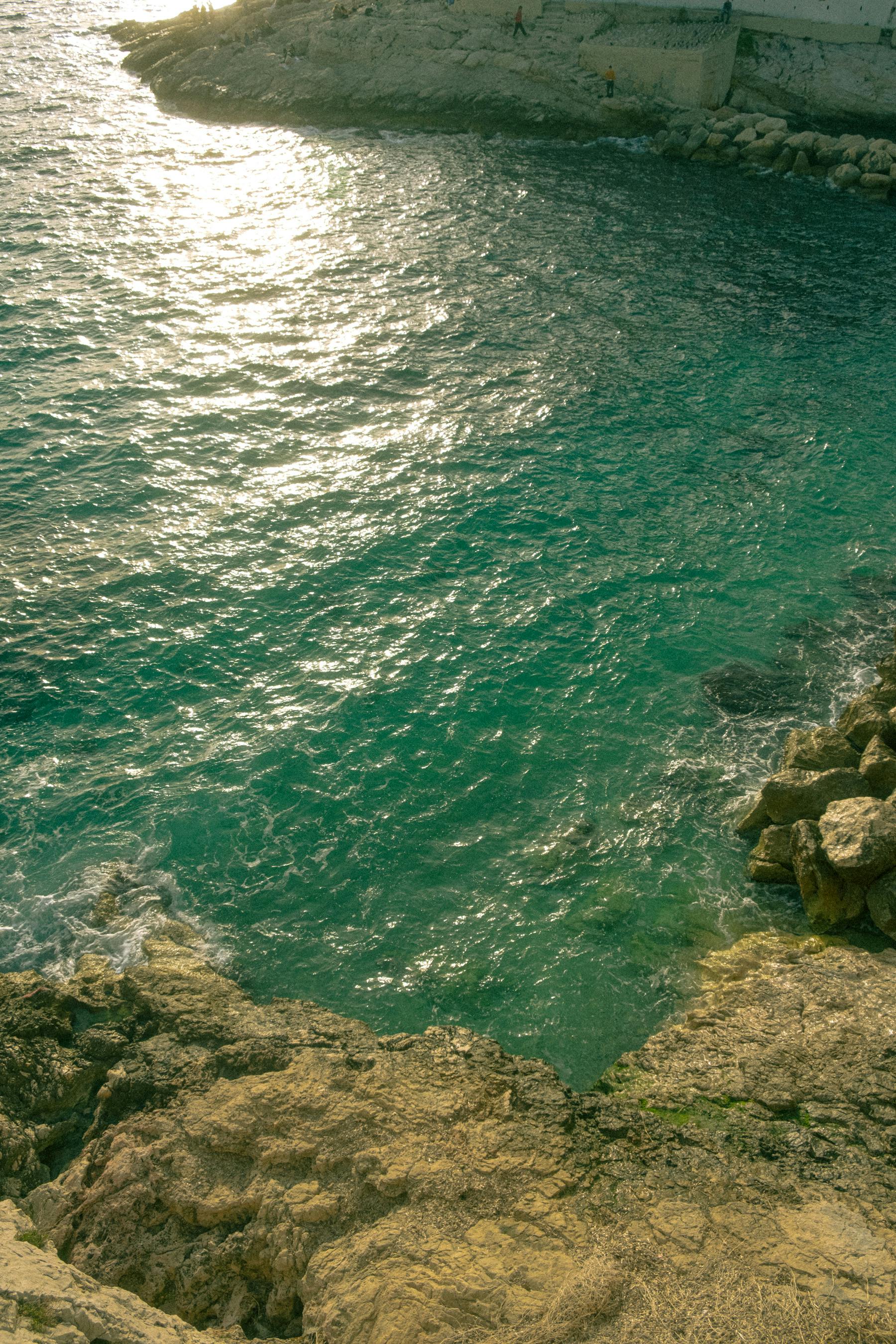 A breathtaking coastal view with sunlit emerald waters, rocky shores, and a bright summer ambiance.