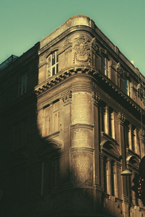 Free A sunlit vintage building's corner in an urban setting with ornate architectural details. Stock Photo