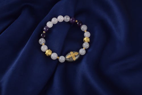 A bracelet with purple and gold beads on a blue cloth