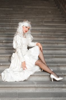 Portrait of a woman in a white dress and crown, sitting elegantly on stairs.