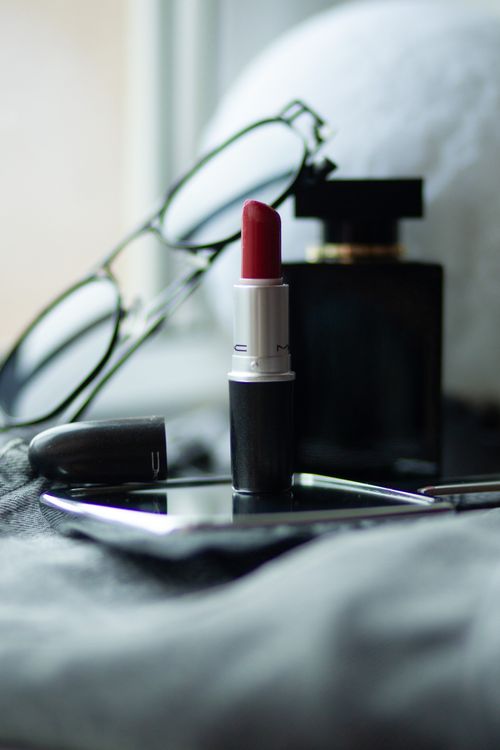 Free A close-up of lipstick, eyeglasses, and perfume on a bed setting, exuding elegance. Stock Photo