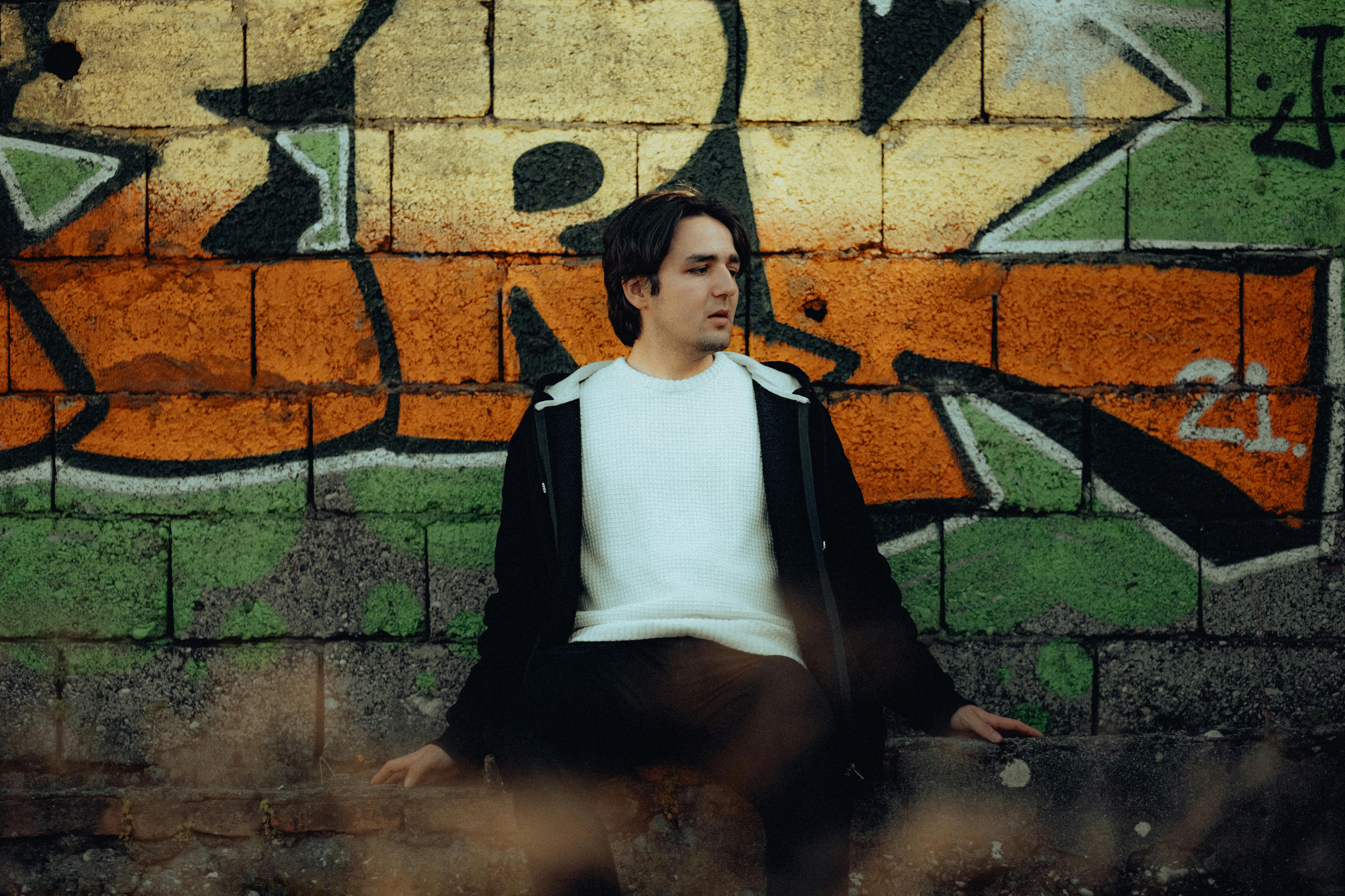 A man sitting on a bench in front of a graffiti wall