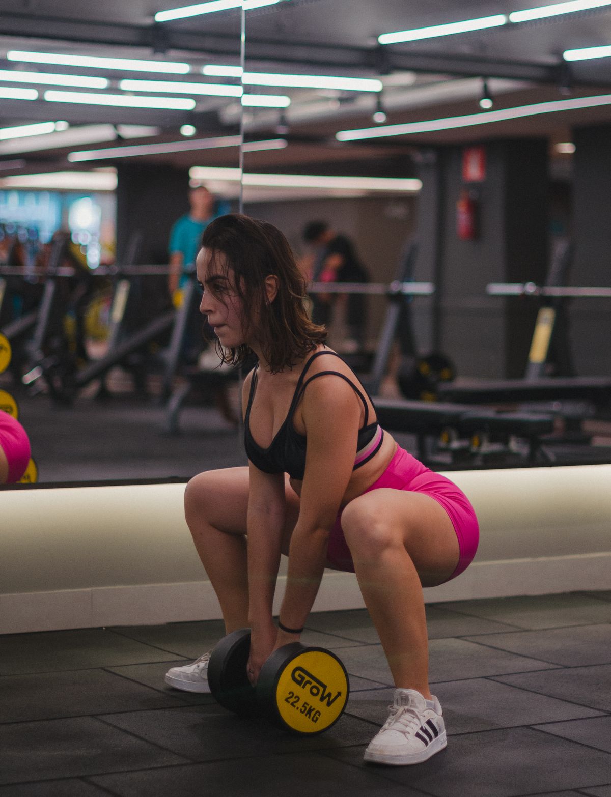 Mulher atlética focada em treino de musculação com barra em academia moderna