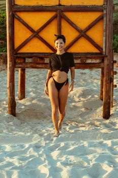 A cheerful woman in beachwear enjoying a sunny day with sand and a wooden structure backdrop.