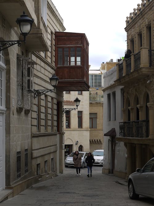 A person walking down a narrow street with a car parked on the side