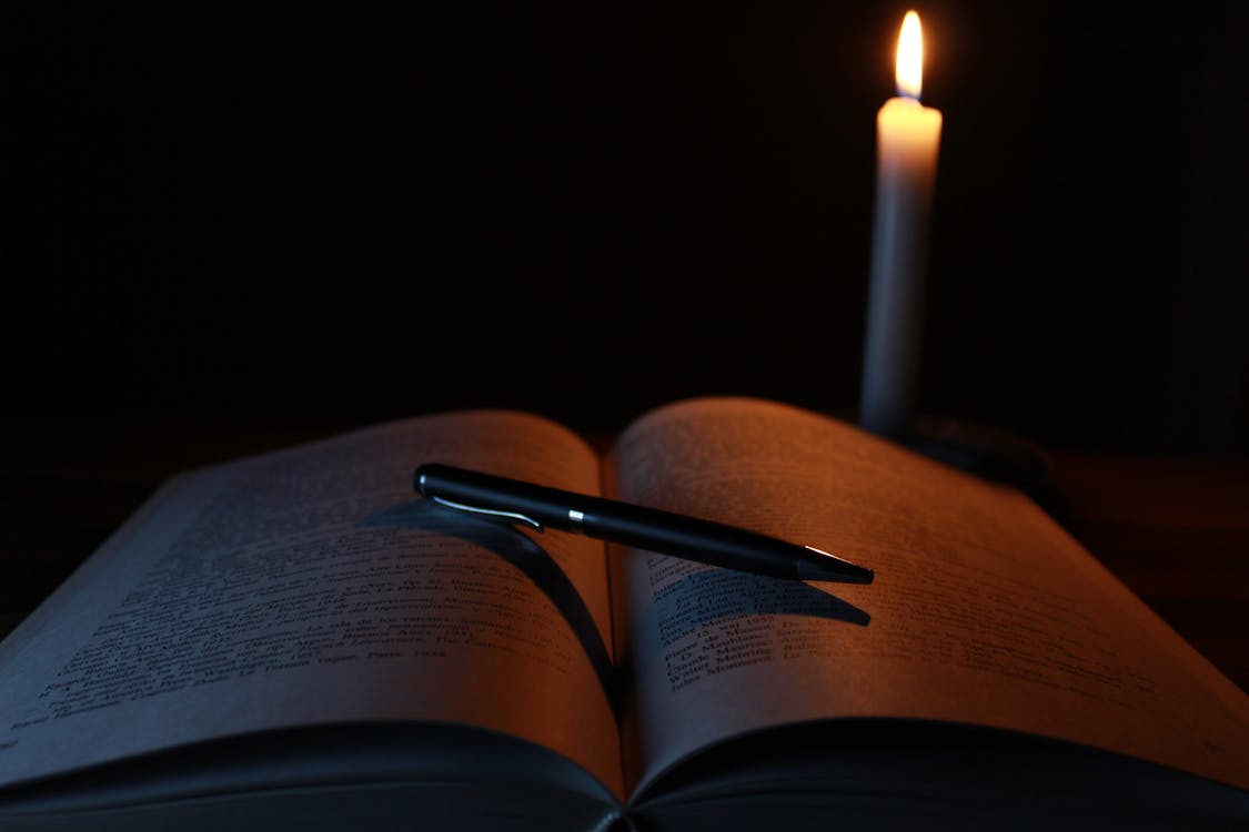 Black Pen on Opened Book Beside Lit Taper Candle