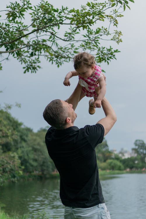 A man holding a baby in the air by a lake