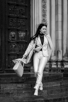Fashionable woman walking down steps with a bag in a black and white urban environment.
