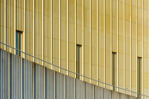 Free Abstract view of a modern building's yellow metallic facade featuring slender windows and a distinctive handrail. Stock Photo
