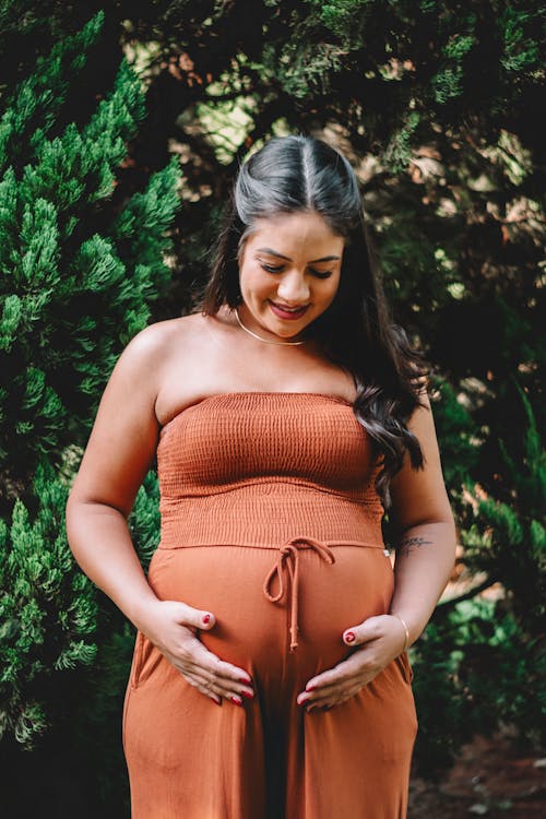 A pregnant woman in a brown dress poses for a maternity photo