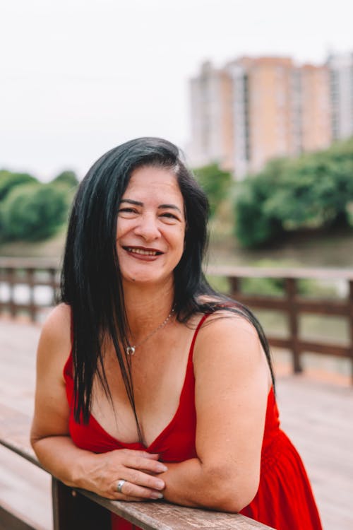 Smiling Woman in Red Dress Standing on Footbridge