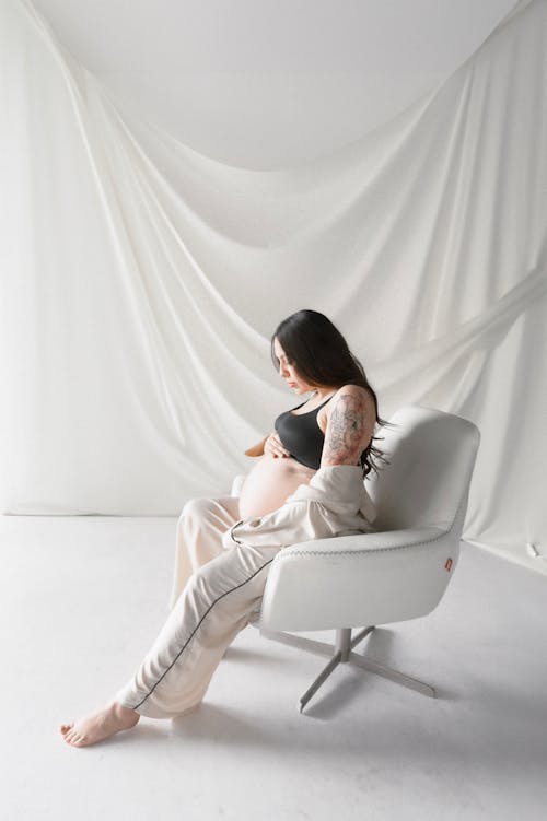 A pregnant woman sitting in a chair with a white curtain behind her