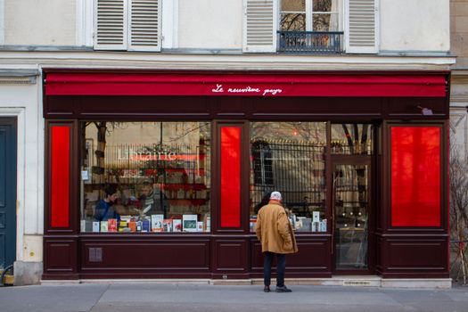 Senior man browsing books at a Parisian storefront with vibrant red accents.