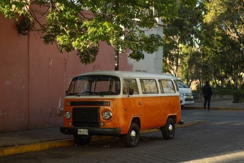 Free Classic orange van parked in a vibrant street of Oaxaca, Mexico, under lush green trees. Stock Photo