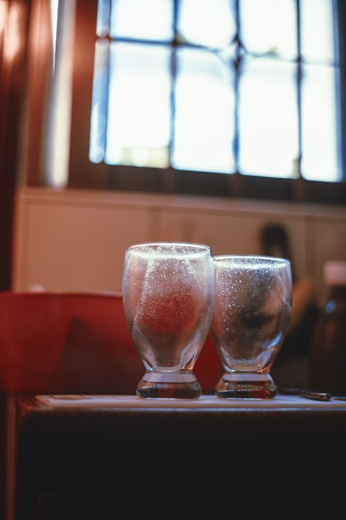 Free Artistic shot of two empty glasses on a tabletop with a window backdrop. Stock Photo