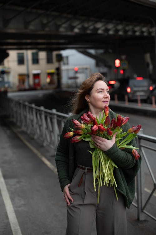 A woman holding a bouquet of flowers under a bridge