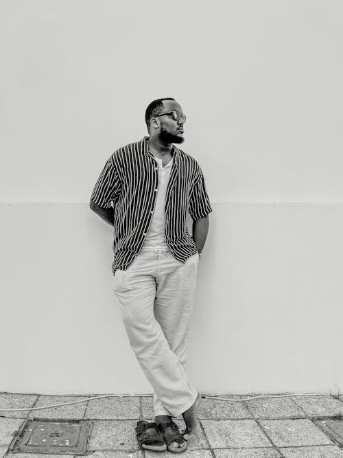 A man standing against a white wall wearing striped pants