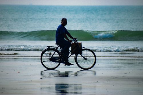 Free A man rides a bicycle along the serene shore of Mandarmani, India with waves in the background. Stock Photo