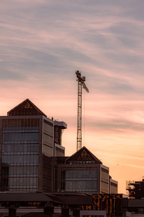 Free City skyline featuring buildings and a construction crane against a sunset sky. Stock Photo