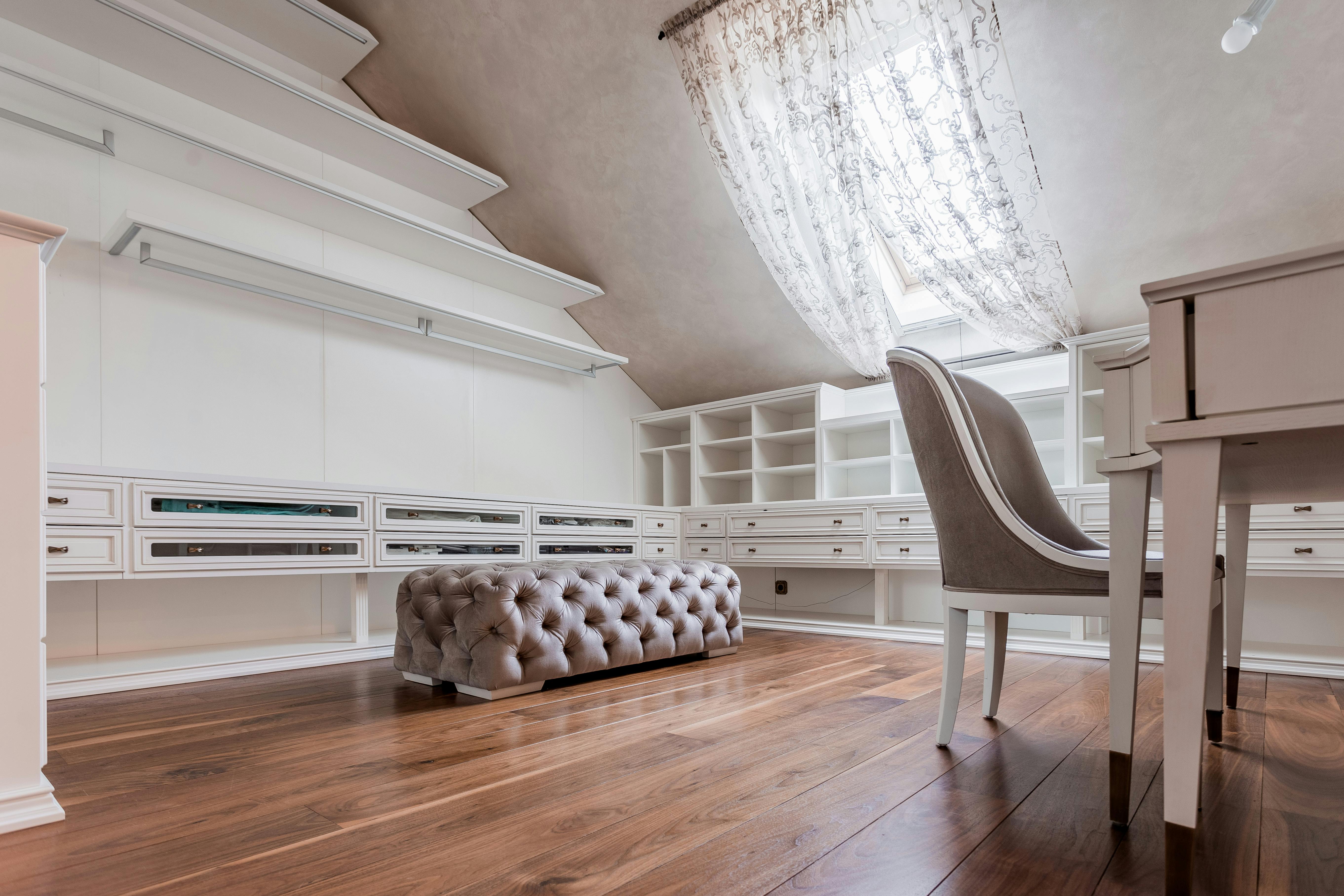 Stylish attic studio featuring a modern desk, pouffe, and sloping ceiling under natural light.