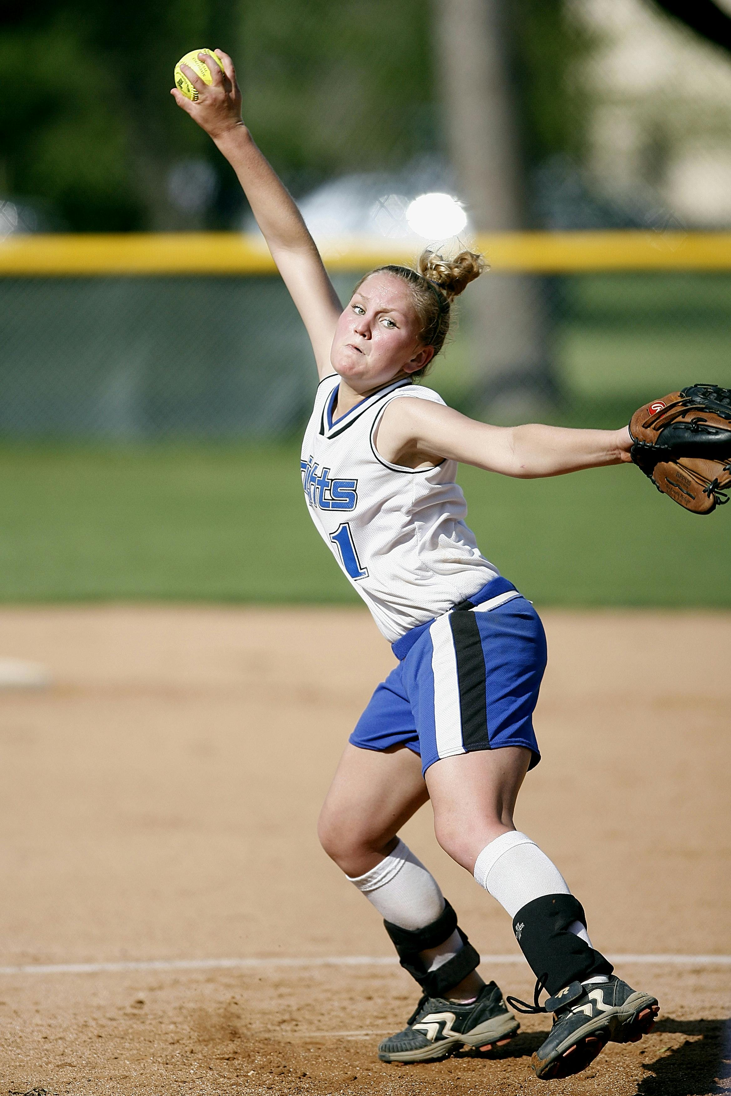 Mixed race female baseball player sitting on bench throwing ball