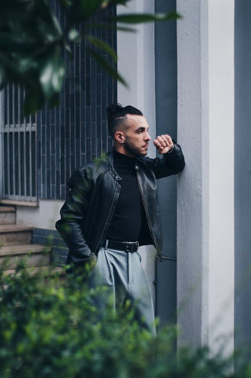 A man leaning against a wall wearing a leather jacket
