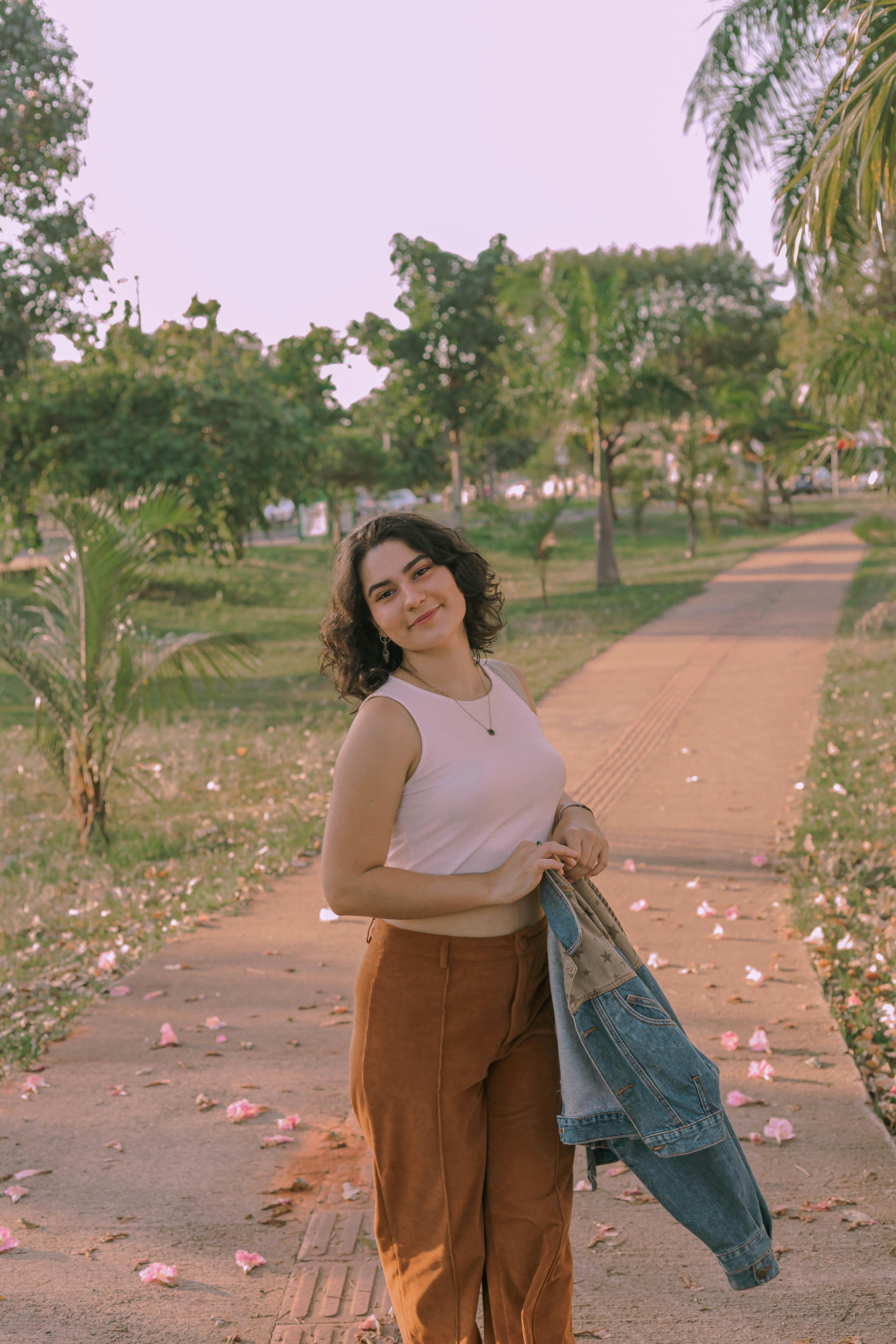 微笑的年轻女子在阳光明媚的公园小径上，在盛开的花朵中摆姿势