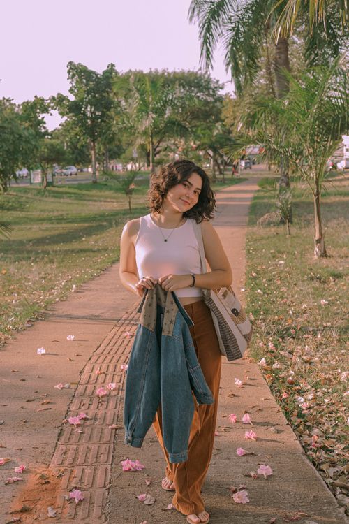 Free A smiling woman walks in a park in Presidente Prudente, Brazil, holding a jacket and showcasing urban fashion. Stock Photo