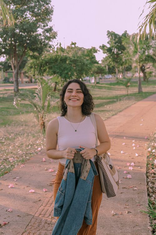 Free A young woman smiling while holding a denim jacket in a sunny park in Presidente Prudente, Brazil. Stock Photo