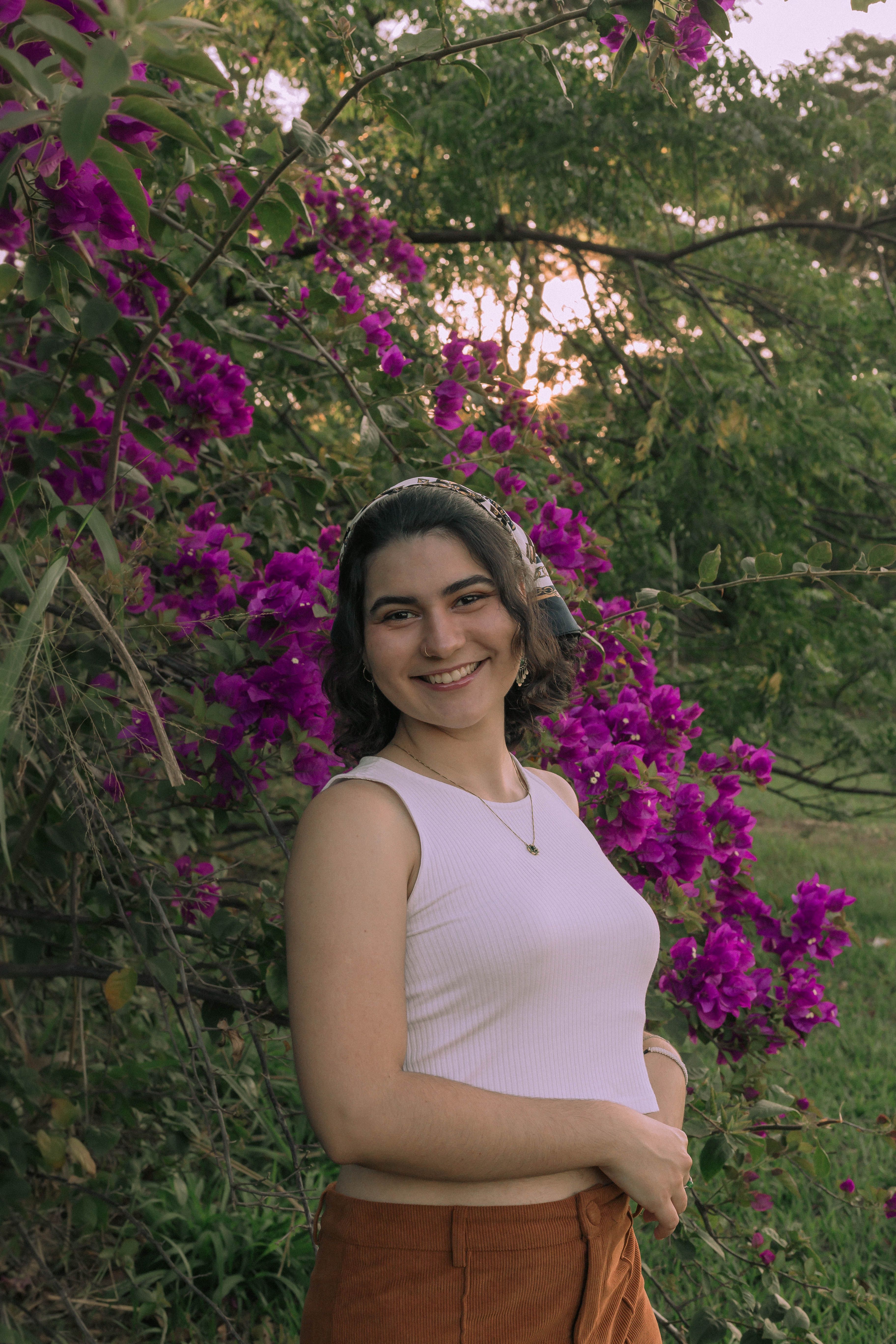 Young woman in a garden, happily posing by vibrant purple flowers under summer light.