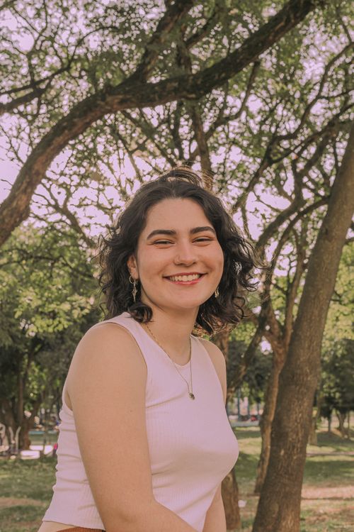 Free Smiling young woman in a white tank top enjoying a sunny day outdoors in a park. Stock Photo
