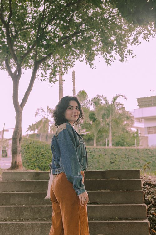 Free Portrait of a fashionable woman standing on steps in a park, wearing a jean jacket. Urban backdrop in Presidente Prudente, Brazil. Stock Photo