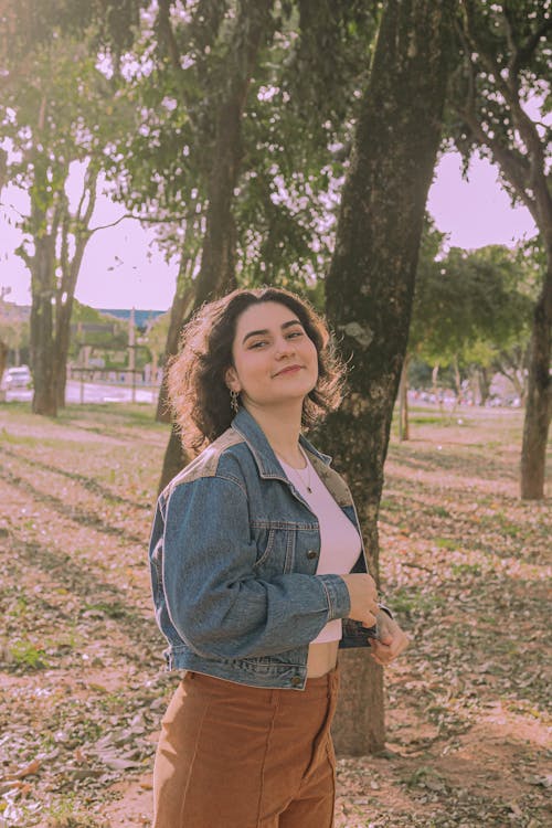A woman in a denim jacket and brown pants standing in a park