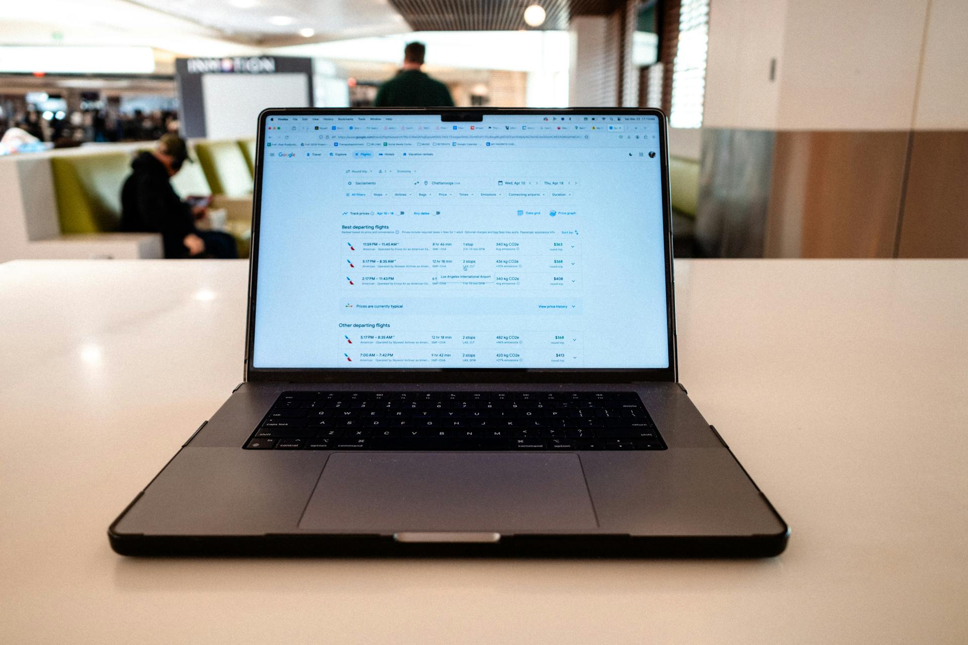 A modern laptop displaying flight schedules on a white table in an airport lounge.