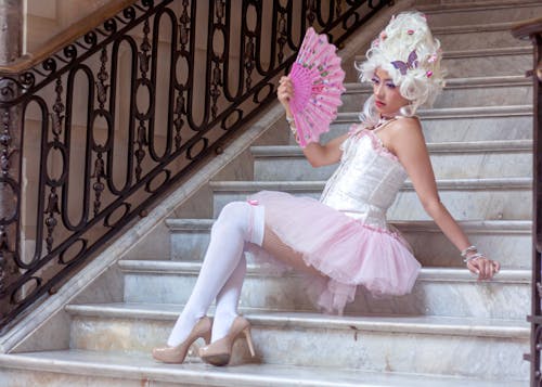 A woman in a pink tutu and white dress sitting on stairs