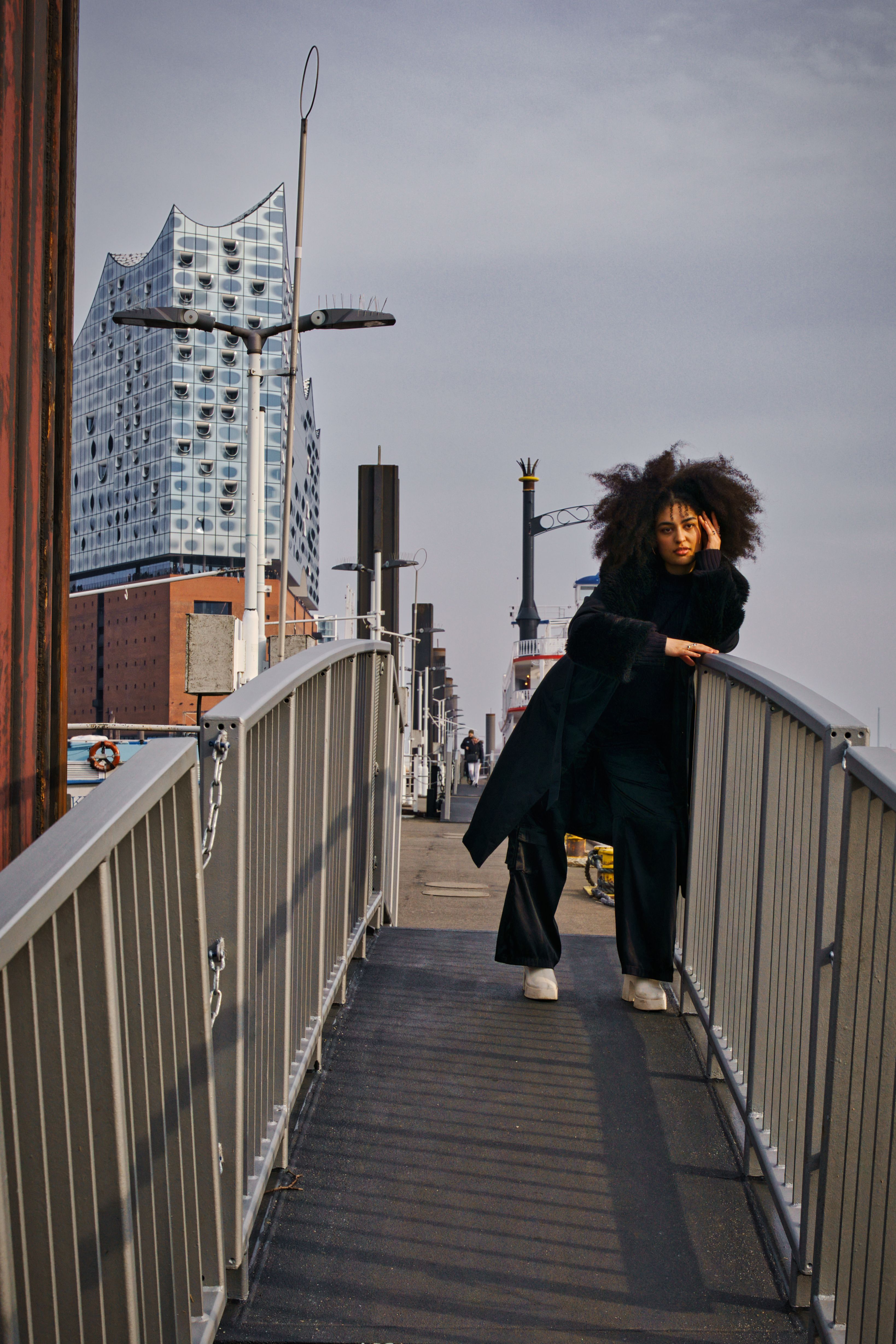 Model posing on a footbridge with Elbphilharmonie in the background, Hamburg.