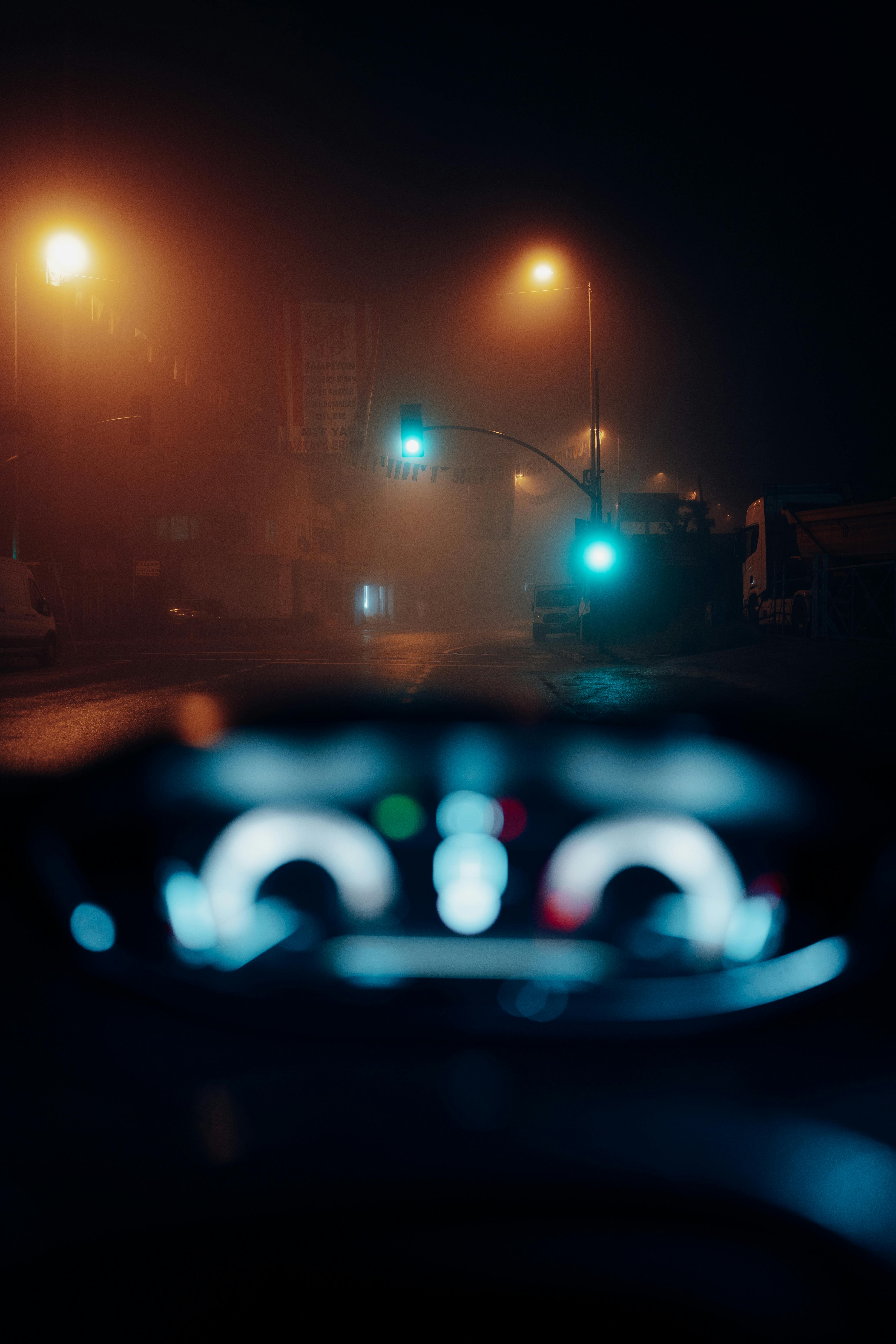 A blurry view from a car dashboard on a foggy city street at night.